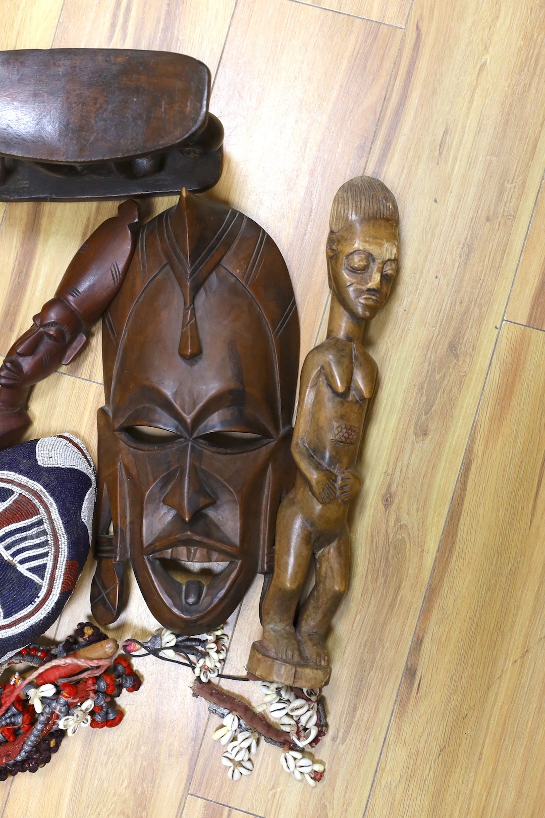 A group of African hardwood carvings, shell and beadwork including a cap